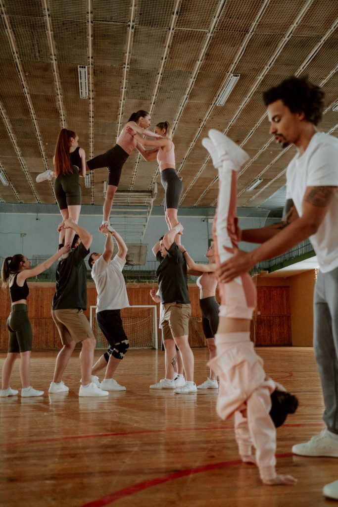 Teenagers and young children practicing gymnastics in a gym under the supervision of a coach.